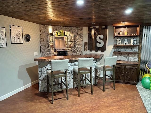 bar featuring wood finished floors, recessed lighting, a bar, wooden ceiling, and baseboards