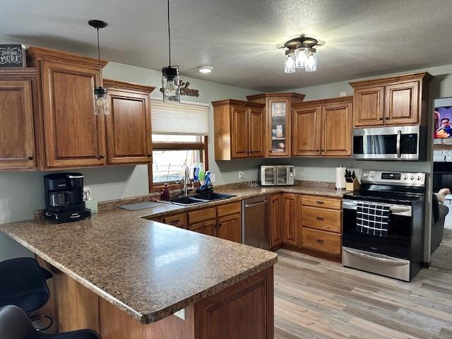 kitchen with a sink, appliances with stainless steel finishes, a breakfast bar area, a peninsula, and brown cabinetry