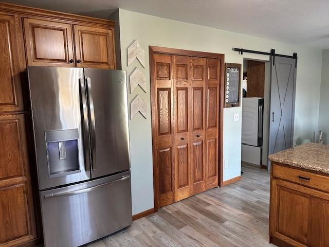 kitchen with brown cabinetry, baseboards, light wood-style floors, stainless steel refrigerator with ice dispenser, and a barn door