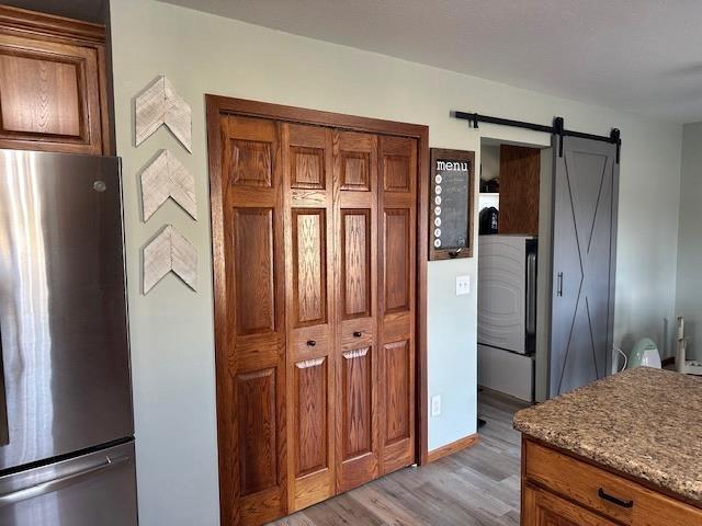 kitchen featuring a barn door, light wood finished floors, brown cabinets, and freestanding refrigerator