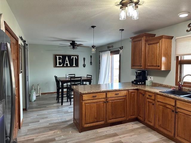 kitchen with light wood-type flooring, brown cabinets, a sink, a barn door, and a peninsula