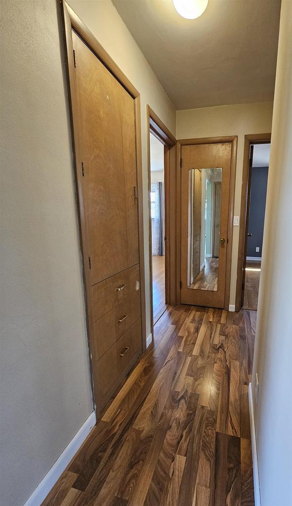 corridor featuring baseboards and dark wood-style flooring