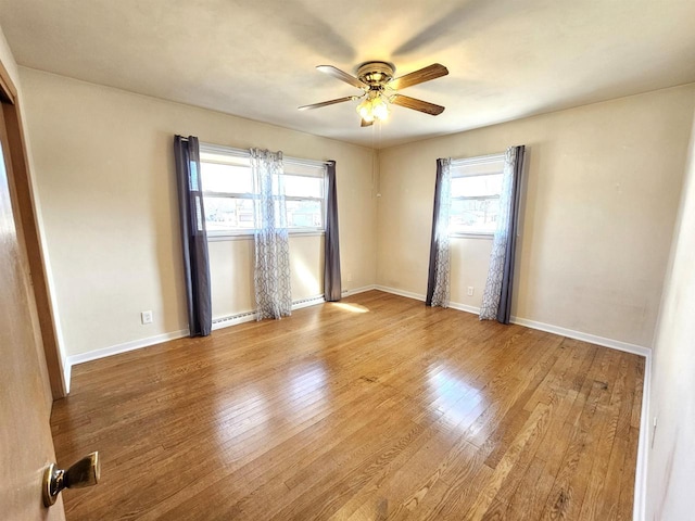 empty room with a baseboard radiator, baseboards, a ceiling fan, and wood-type flooring