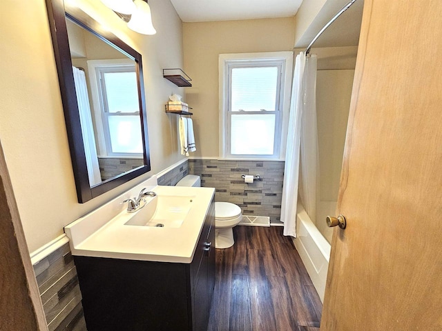 full bath featuring a wealth of natural light, a wainscoted wall, toilet, and tile walls