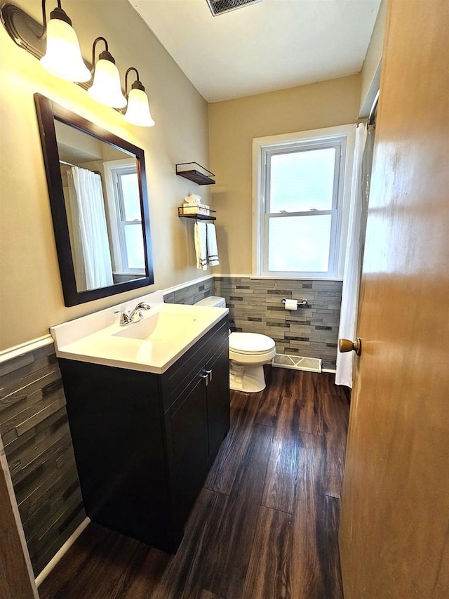 bathroom featuring vanity, wood finished floors, a wainscoted wall, tile walls, and toilet