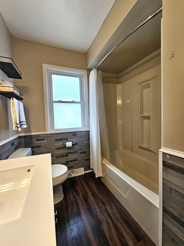 full bath featuring toilet, shower / bath combo, wood finished floors, tile walls, and wainscoting