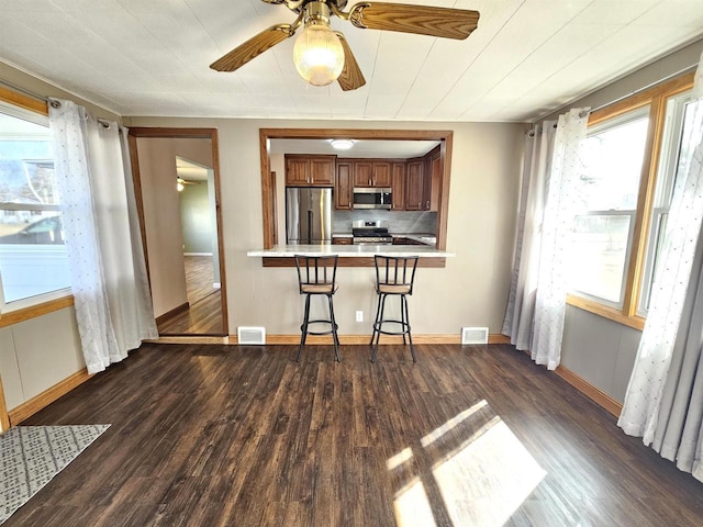 kitchen featuring a kitchen bar, dark wood-type flooring, brown cabinetry, and stainless steel appliances