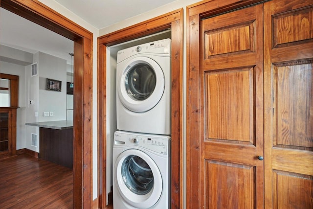 laundry area featuring stacked washer / drying machine, visible vents, dark wood finished floors, and laundry area