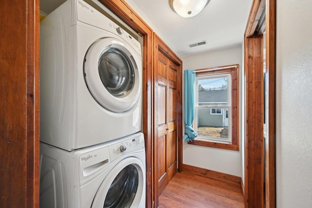 laundry area featuring visible vents, stacked washer and clothes dryer, baseboards, and wood finished floors