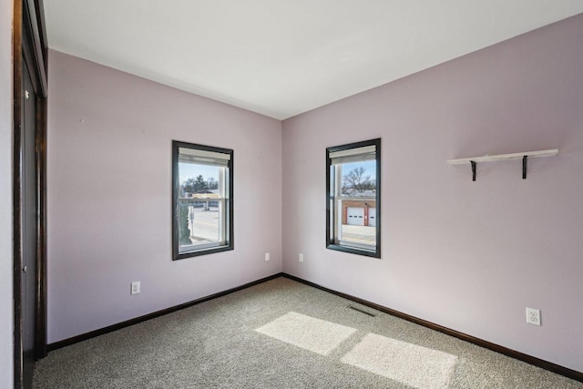 empty room with a wealth of natural light, visible vents, baseboards, and carpet