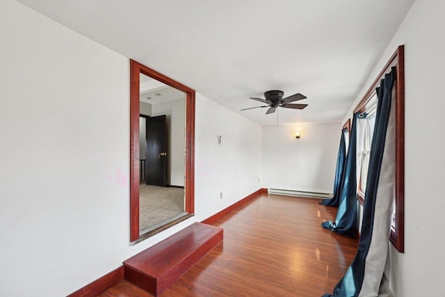 empty room featuring baseboard heating, a ceiling fan, baseboards, and wood finished floors