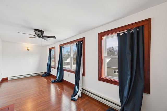 unfurnished room featuring a baseboard radiator, baseboards, wood finished floors, and a ceiling fan