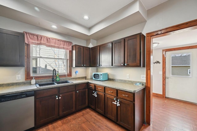 kitchen with dark brown cabinetry, dishwasher, wood finished floors, and a sink