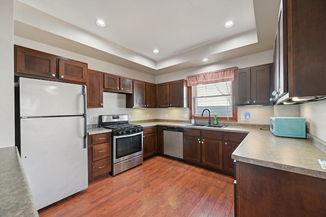 kitchen featuring dark wood-type flooring, recessed lighting, appliances with stainless steel finishes, a raised ceiling, and a sink