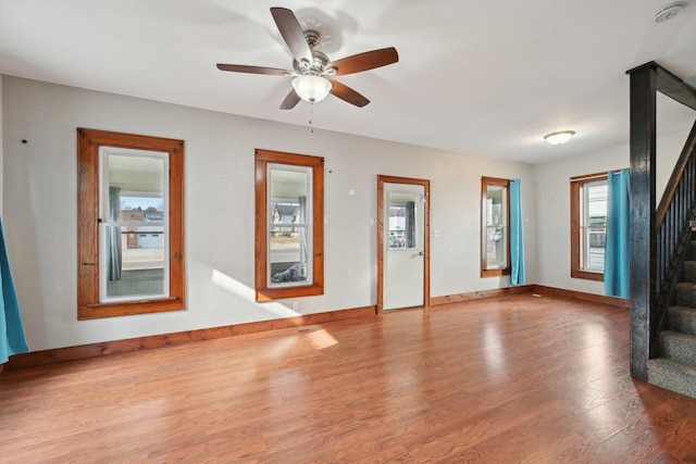 unfurnished living room with stairway, wood finished floors, baseboards, and ceiling fan