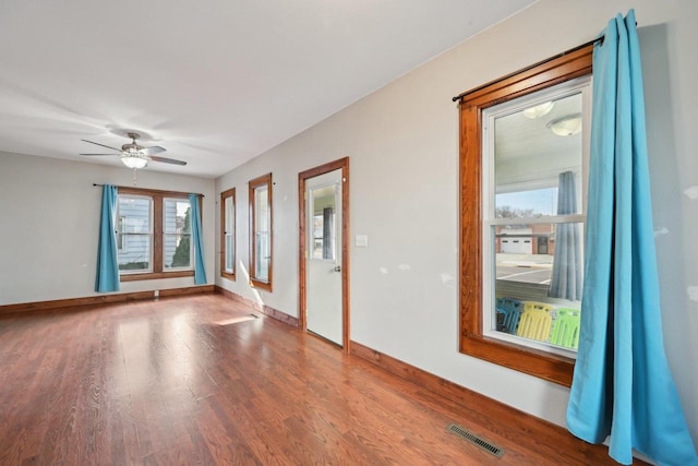 empty room with ceiling fan, visible vents, baseboards, and wood finished floors