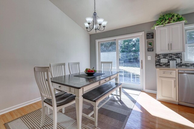 dining room featuring vaulted ceiling, light wood-style flooring, a notable chandelier, and baseboards