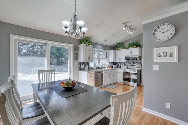 dining room featuring track lighting, baseboards, lofted ceiling, light wood-style floors, and a notable chandelier