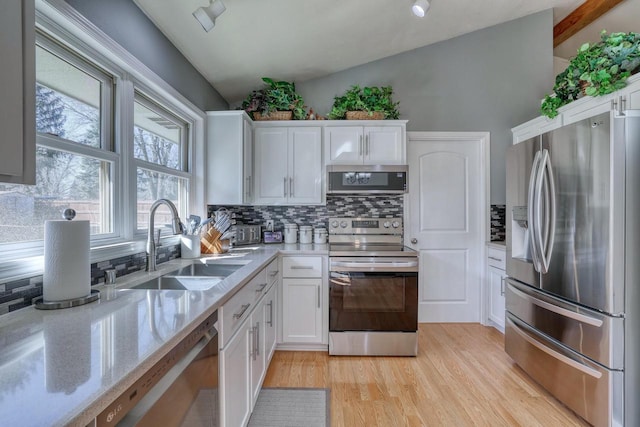 kitchen with a sink, stainless steel appliances, vaulted ceiling, white cabinets, and light wood-type flooring