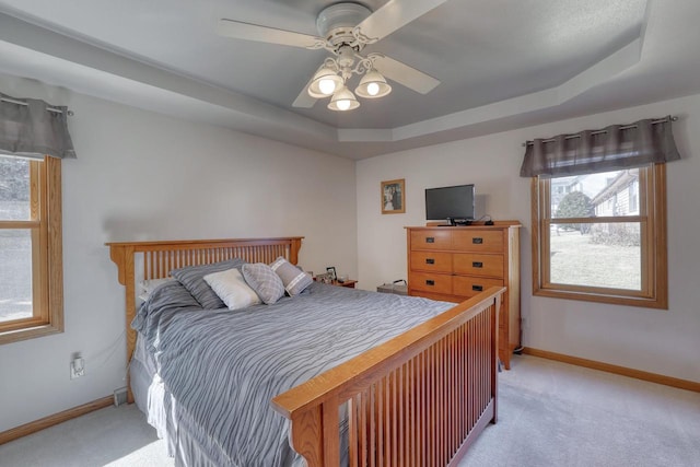 bedroom featuring light carpet, a raised ceiling, and baseboards