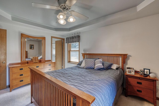 bedroom featuring a tray ceiling, light carpet, and ceiling fan