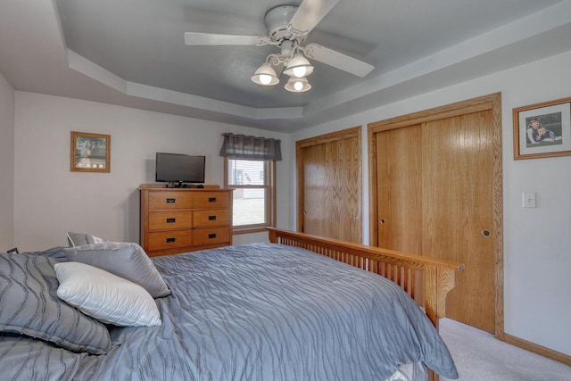 carpeted bedroom with a raised ceiling, baseboards, two closets, and ceiling fan