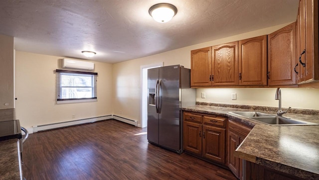 kitchen featuring dark countertops, dark wood finished floors, a wall unit AC, stainless steel fridge, and a sink