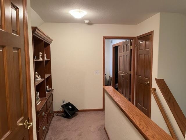 hallway featuring baseboards, an upstairs landing, and carpet flooring