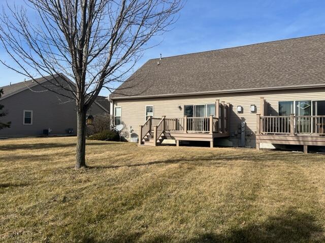 back of house featuring a lawn, roof with shingles, and a deck