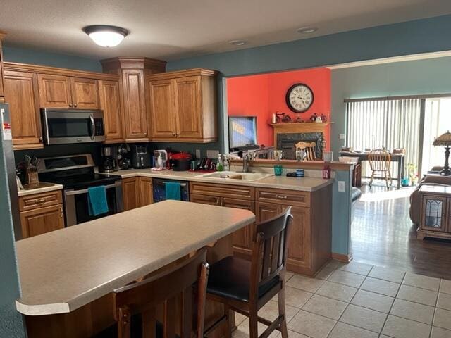 kitchen with light countertops, a peninsula, light tile patterned flooring, stainless steel appliances, and a sink