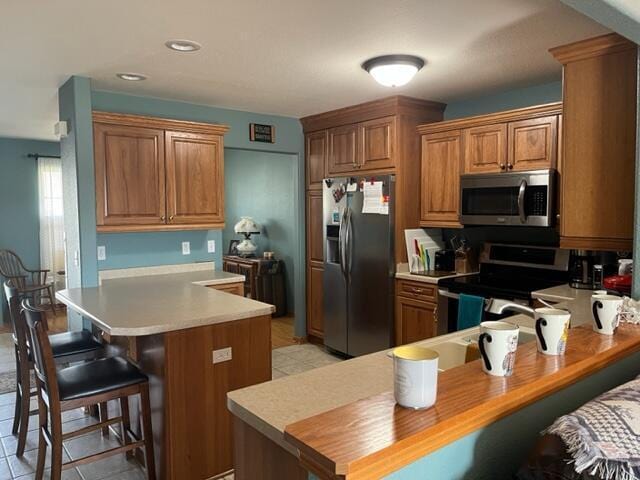 kitchen featuring a breakfast bar, a peninsula, brown cabinetry, and stainless steel appliances