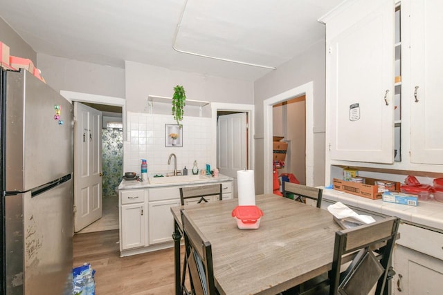 kitchen featuring freestanding refrigerator, a sink, decorative backsplash, white cabinets, and light wood-type flooring