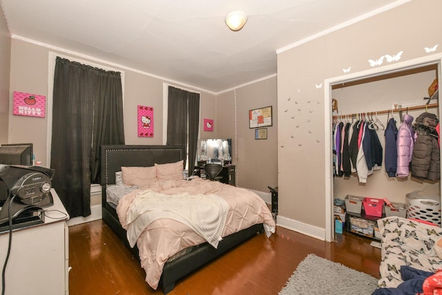 bedroom featuring a closet, baseboards, wood finished floors, and crown molding