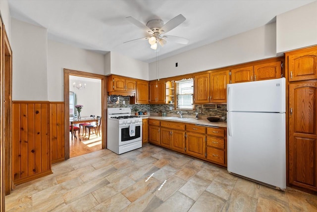 kitchen featuring white appliances, brown cabinetry, a wainscoted wall, a sink, and light countertops