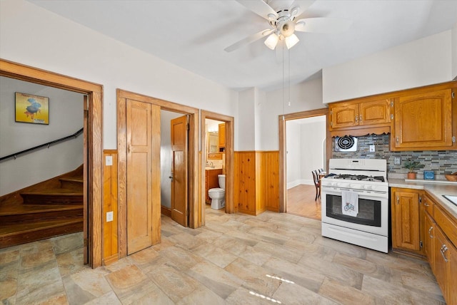 kitchen with a wainscoted wall, brown cabinets, wooden walls, light countertops, and white gas range