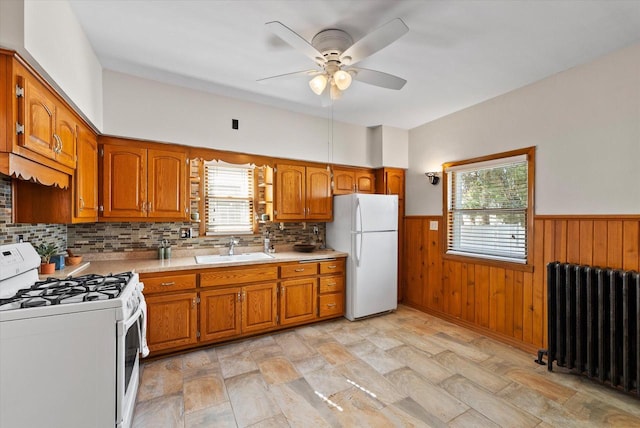 kitchen with a sink, white appliances, radiator, and brown cabinetry