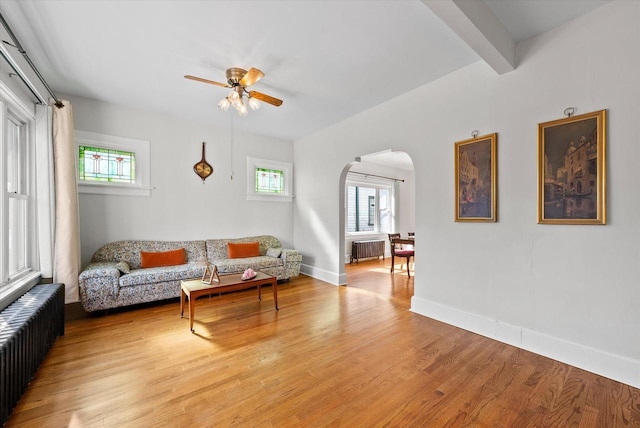 living room with light wood-type flooring, arched walkways, baseboards, and radiator heating unit