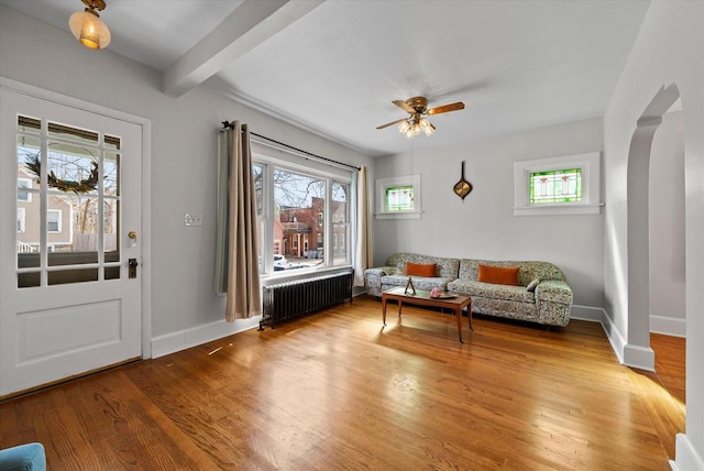 sitting room featuring beam ceiling, radiator heating unit, arched walkways, light wood finished floors, and baseboards