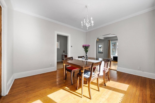 dining space featuring a notable chandelier, arched walkways, crown molding, light wood finished floors, and baseboards