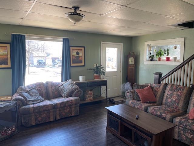 living area featuring dark wood-type flooring, stairway, and a drop ceiling