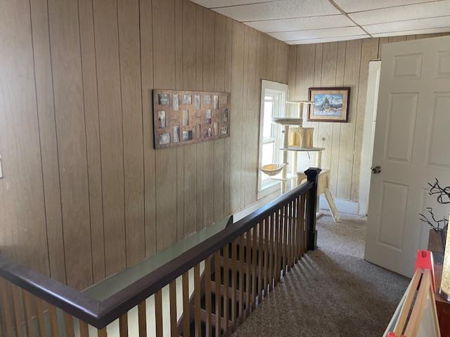 corridor with an upstairs landing, carpet floors, and wood walls