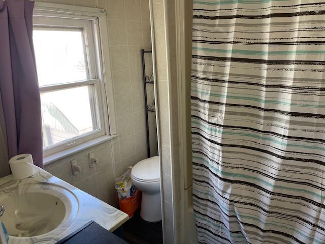 full bathroom featuring a shower with shower curtain, toilet, tile walls, and vanity