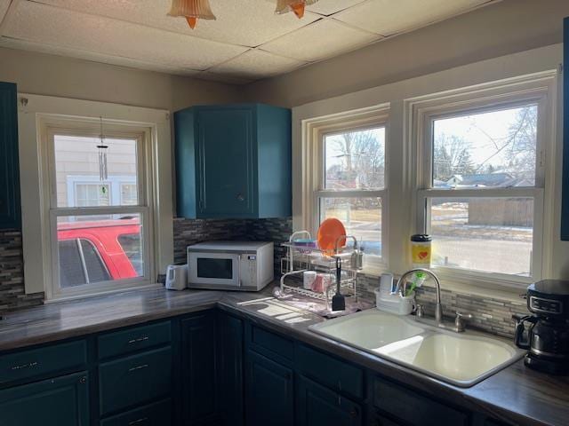 kitchen with white microwave, tasteful backsplash, blue cabinetry, a drop ceiling, and a sink