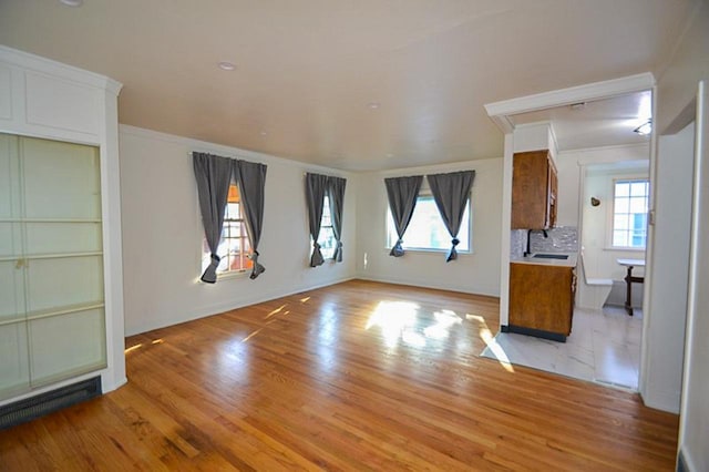 unfurnished living room with ornamental molding, light wood-style floors, visible vents, and a sink