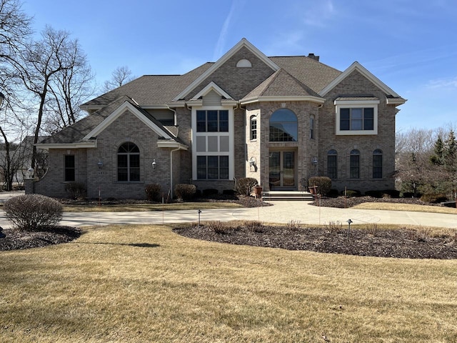 view of front of property with brick siding, a chimney, a front lawn, and roof with shingles