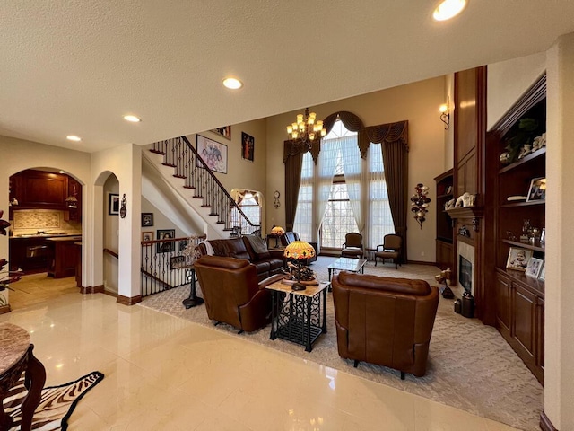 living room featuring stairway, recessed lighting, a textured ceiling, a glass covered fireplace, and a chandelier