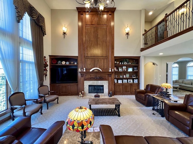 living area featuring a high end fireplace, built in shelves, decorative columns, a towering ceiling, and arched walkways