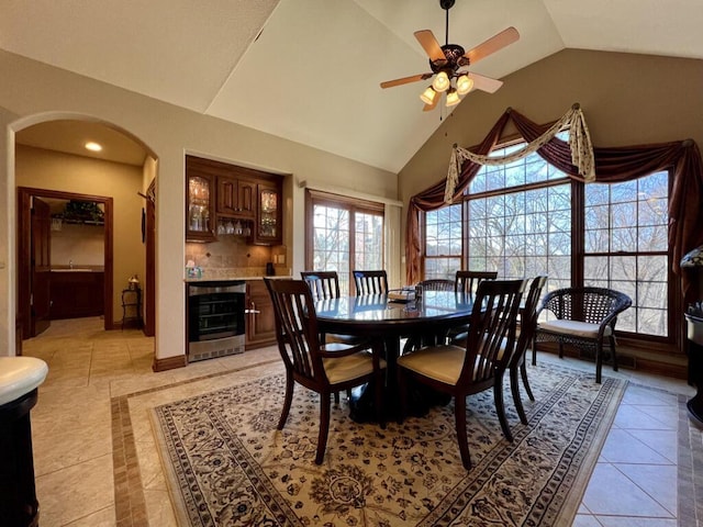 dining area with beverage cooler, baseboards, lofted ceiling, arched walkways, and a dry bar