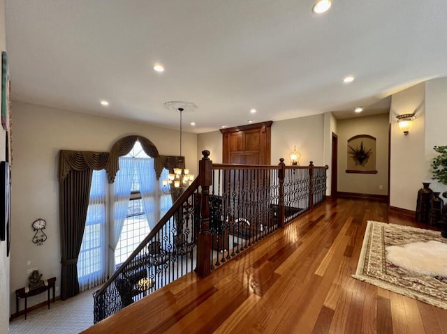 hallway with an upstairs landing, wood finished floors, recessed lighting, an inviting chandelier, and baseboards