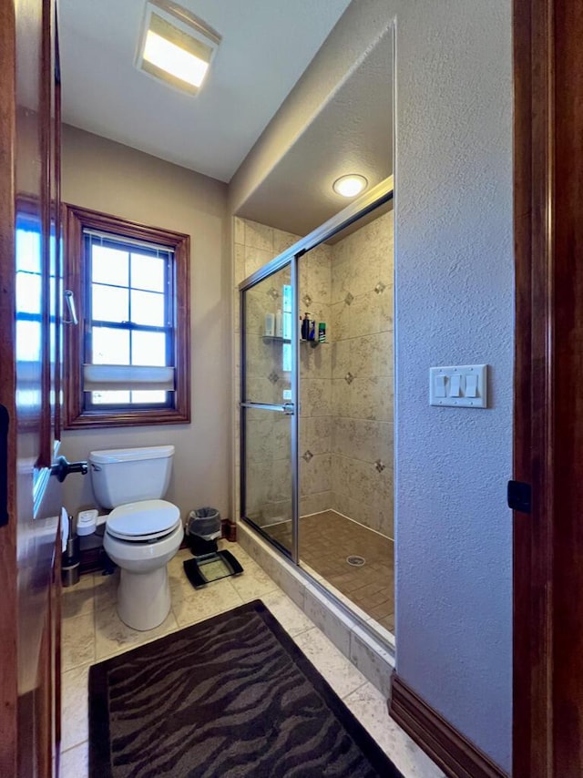 full bathroom featuring tile patterned floors, toilet, a stall shower, baseboards, and a textured wall